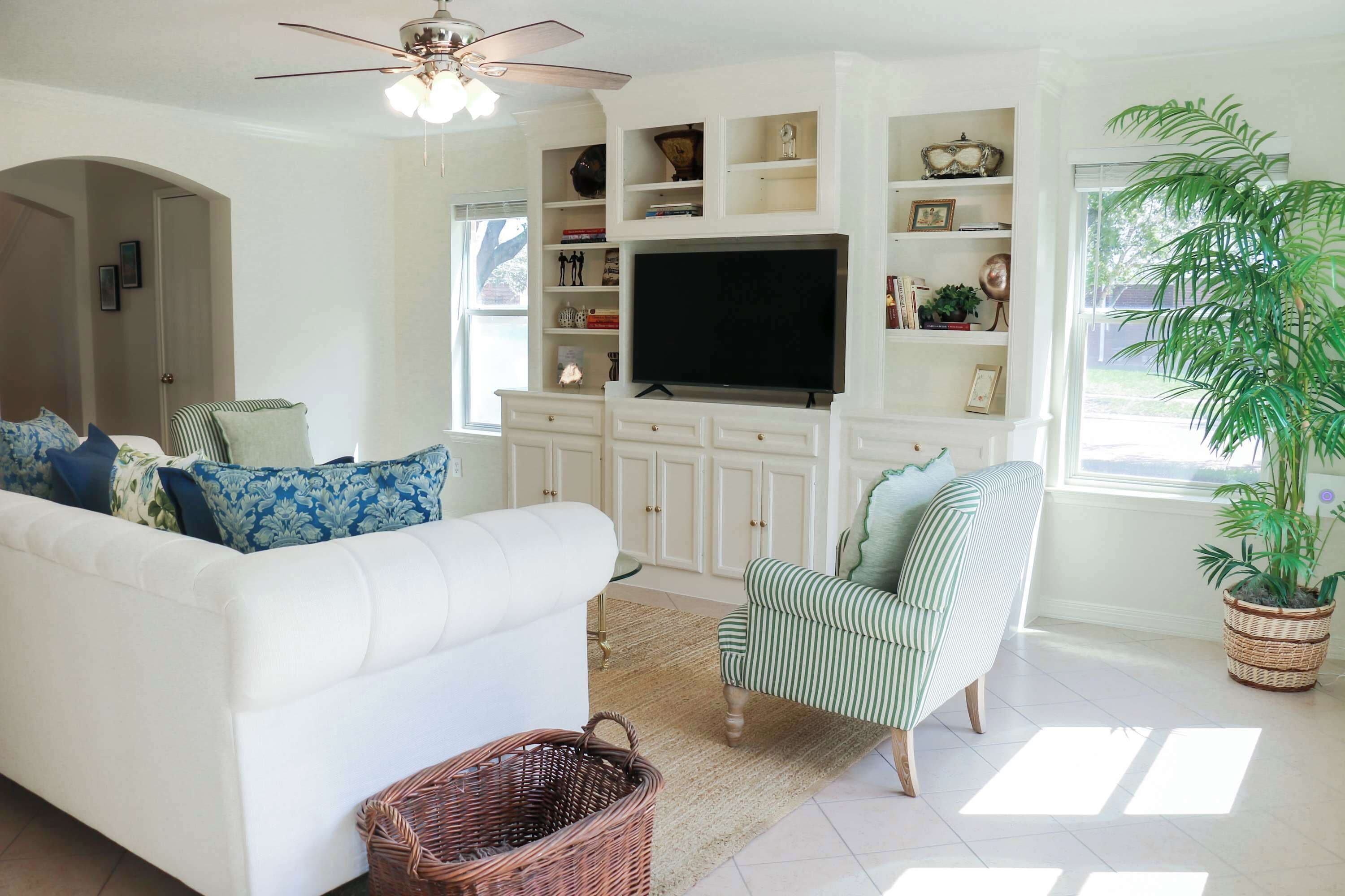 A living room with a white sofa, a striped armchair, a television, and a large plant.