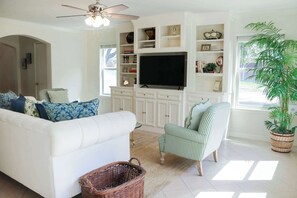 A living room with a white sofa, a striped armchair, a television, and a large plant. - 3-BD/2.5-BA Charming Getaway, Only 10 mins to DT! (Houston)