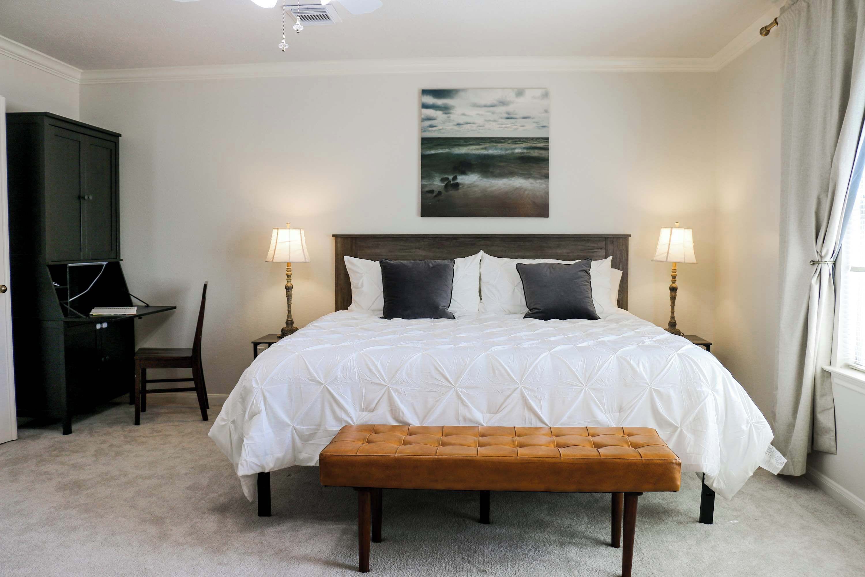 A bedroom with a large bed, two bedside lamps, a desk, and a bench.