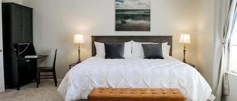 A bedroom with a large bed, two bedside lamps, a desk, and a bench.