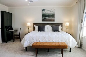Een slaapkamer met een groot bed, twee bedlampen, een bureau en een bankje.