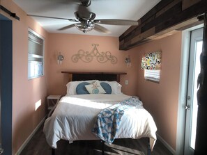 Ein Schlafzimmer mit einem Bett, einem Deckenventilator, einem Fenster mit Jalousien und einer Tür.