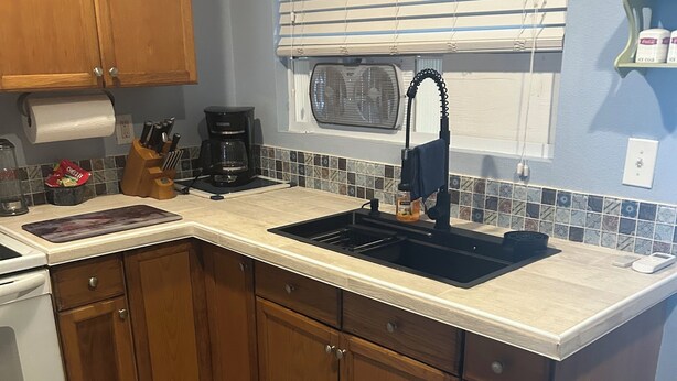 A kitchen with wooden cabinets, a double sink, a stove, and a window with blinds. - Cozy cottage in charming St. Cloud perfect for your getaway. (St. Cloud)