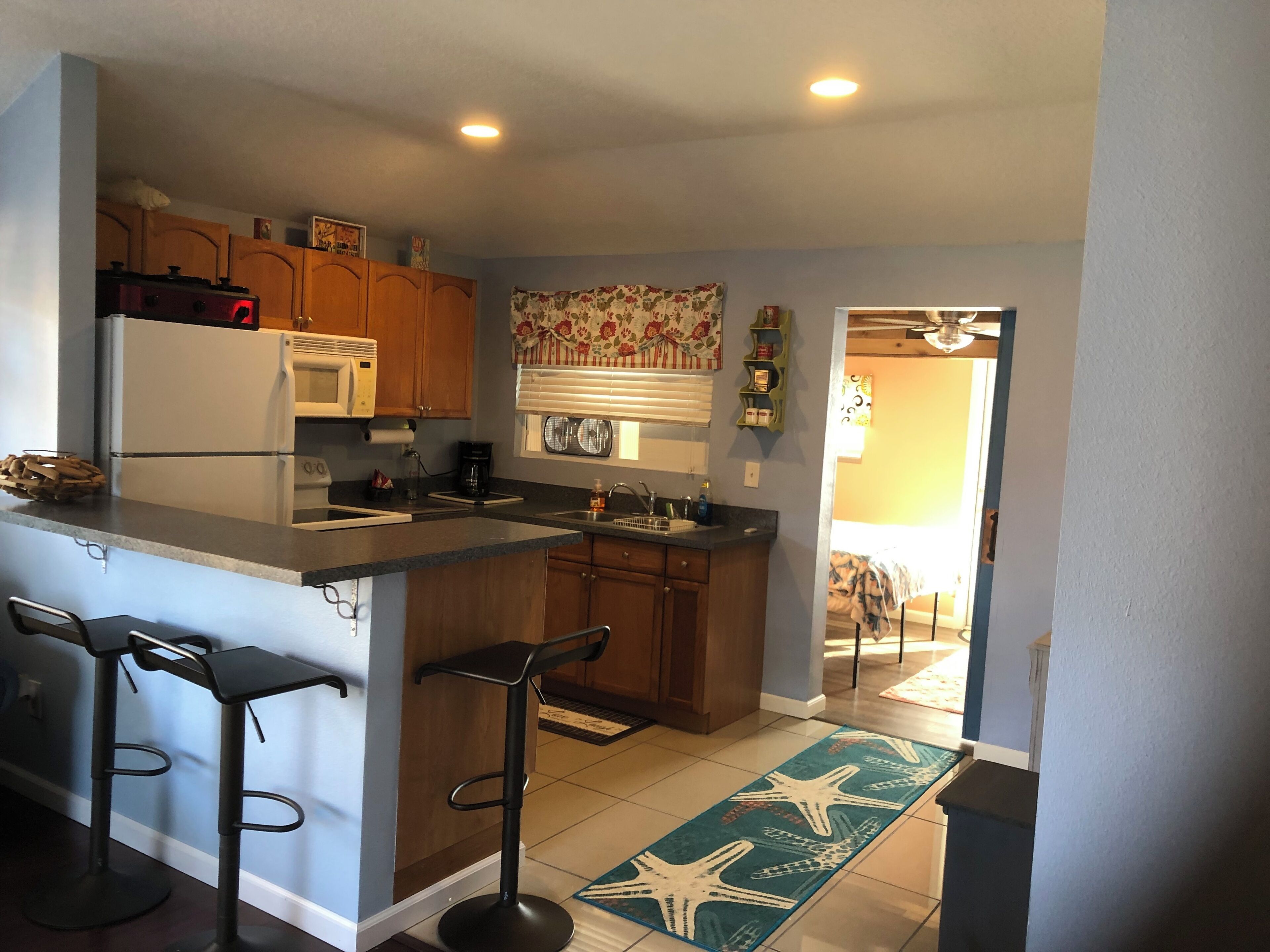Una cocina con refrigerador, microondas, cafetera y dos taburetes de bar.