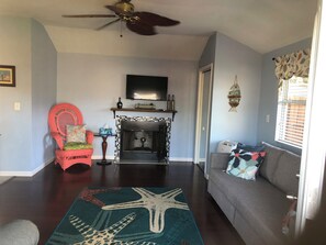 A living room with a fireplace, a ceiling fan, a television, and a sofa.