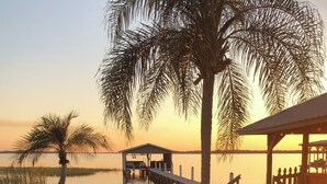 A dock extending into calm water with a covered seating area and a palm tree. - Cozy cottage in charming St. Cloud perfect for your getaway. (St. Cloud)
