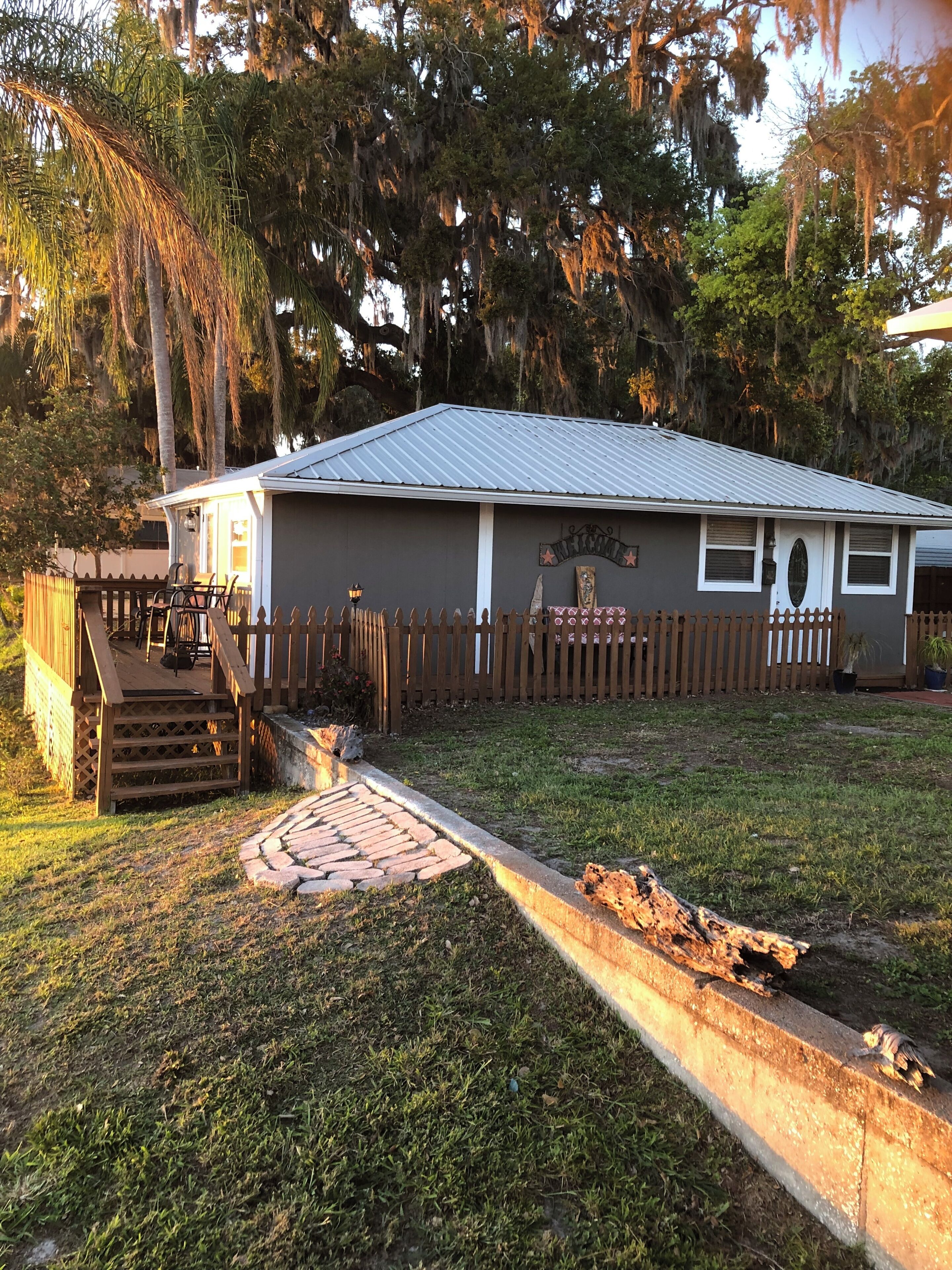 A small house with a porch, a wooden fence, and a sign that reads 'WELCOME'.