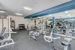 Un gimnasio con equipo de ejercicio variado, incluyendo máquinas de pesas y pesas libres, y un espejo grande en la pared.