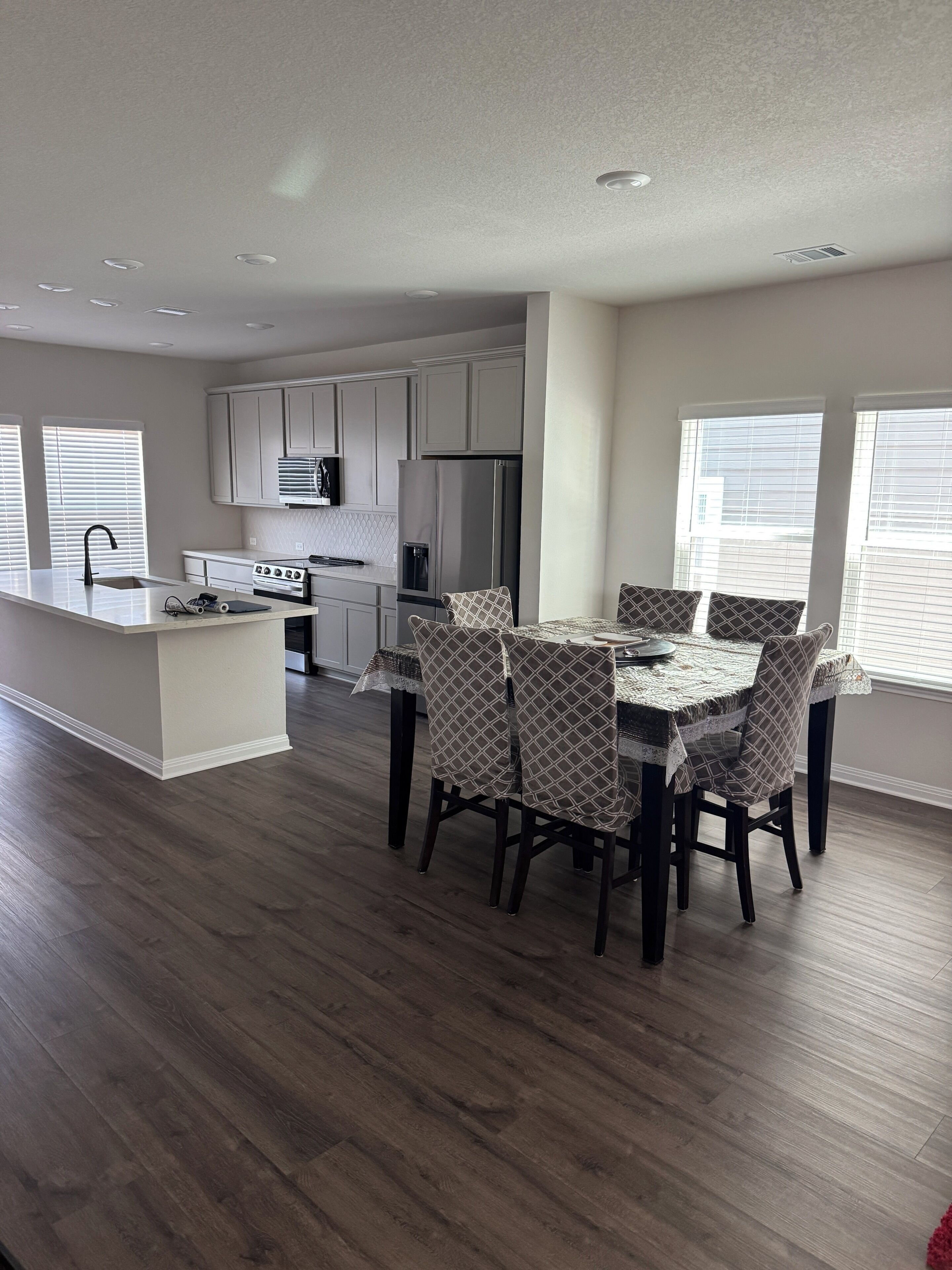 A modern kitchen with white cabinets, a stainless steel refrigerator, and a dining area with patterned chairs and a table.