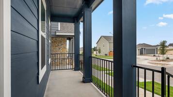 A covered outdoor balcony with a stone wall, metal railing, and a view of a residential street.