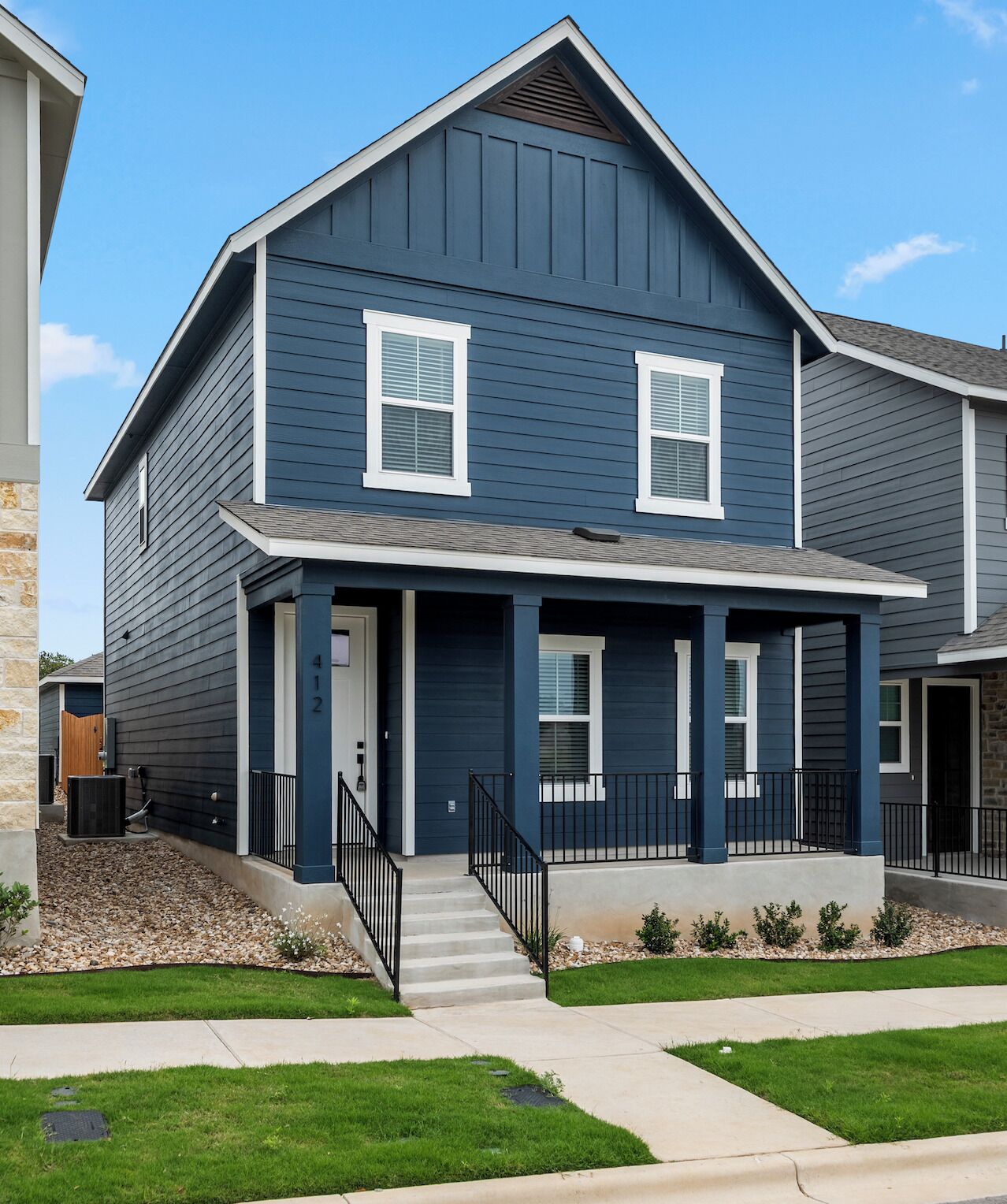 A two-story residential building with a dark blue exterior, white trim, and a front porch with steps leading to the entrance.