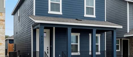 A two-story residential building with a dark blue exterior, white trim, and a front porch with steps leading to the entrance.