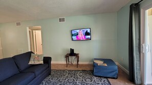 Ein Wohnzimmer mit an der Wand montiertem Fernseher, einer Couch, einem Couchtisch und einem gemusterten Teppich.