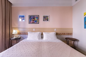 Ein Hotelzimmer mit einem großen Bett, einem Nachttisch mit Lampe und drei gerahmten Kunstwerken an der Wand.
