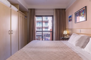 Ein Hotelzimmer mit einem großen Bett, einem Schrank, einem Balkon mit Stühlen und zwei gerahmten Kunstwerken an der Wand.