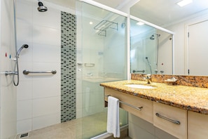 Ein modernes Badezimmer mit einer Duschkabine aus Glas, einem Waschbecken mit Granitplatte und einem großen Spiegel.