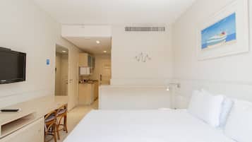 Een hotelkamer met een bed, een televisie, een bureau met stoelen, en een kitchenette op de achtergrond.