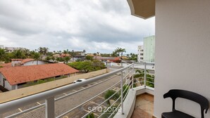 En balkon med udsigt over en gade og bygninger, et hvidt gelænder og en sort stol.