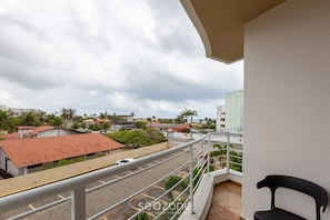 Ein Balkon mit Blick auf eine Straße und Gebäude, mit einem weißen Geländer und einem schwarzen Stuhl.