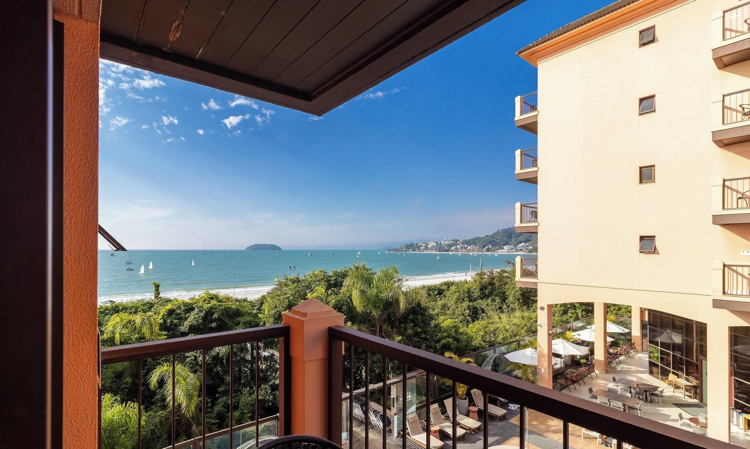 A balcony with a view of the sea, a building with multiple floors, and outdoor seating.