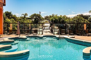 A swimming pool with a glass barrier, lounge chairs, and a view of a natural landscape. - Ocean View Studio in Luxury Resort - Jurere Jbv124 (Florianópolis)
