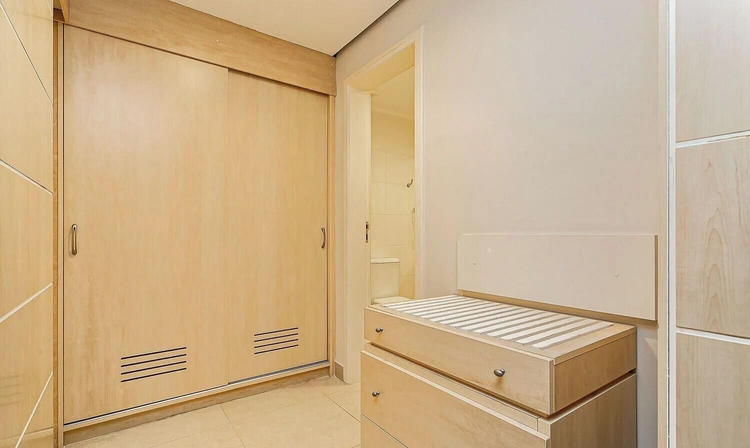 A bedroom with a wooden wardrobe, a bed with a headboard, and a mirror.