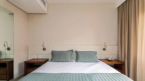 A hotel room with a bed, two bedside tables, a wall-mounted phone, and a window with curtains. - Apt W/pool in Luxury Resort in Jurere Jbv167 (Florianópolis)