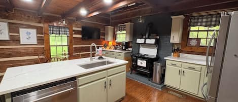 Una cocina con vigas de madera, una isla central con un fregadero, una estufa y un refrigerador.