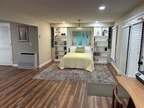 A bedroom with a bed, a bookshelf, a radiator, and a door with blinds.