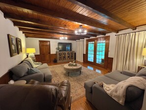 A cozy living room with a wooden ceiling, a television, and a large window with curtains.