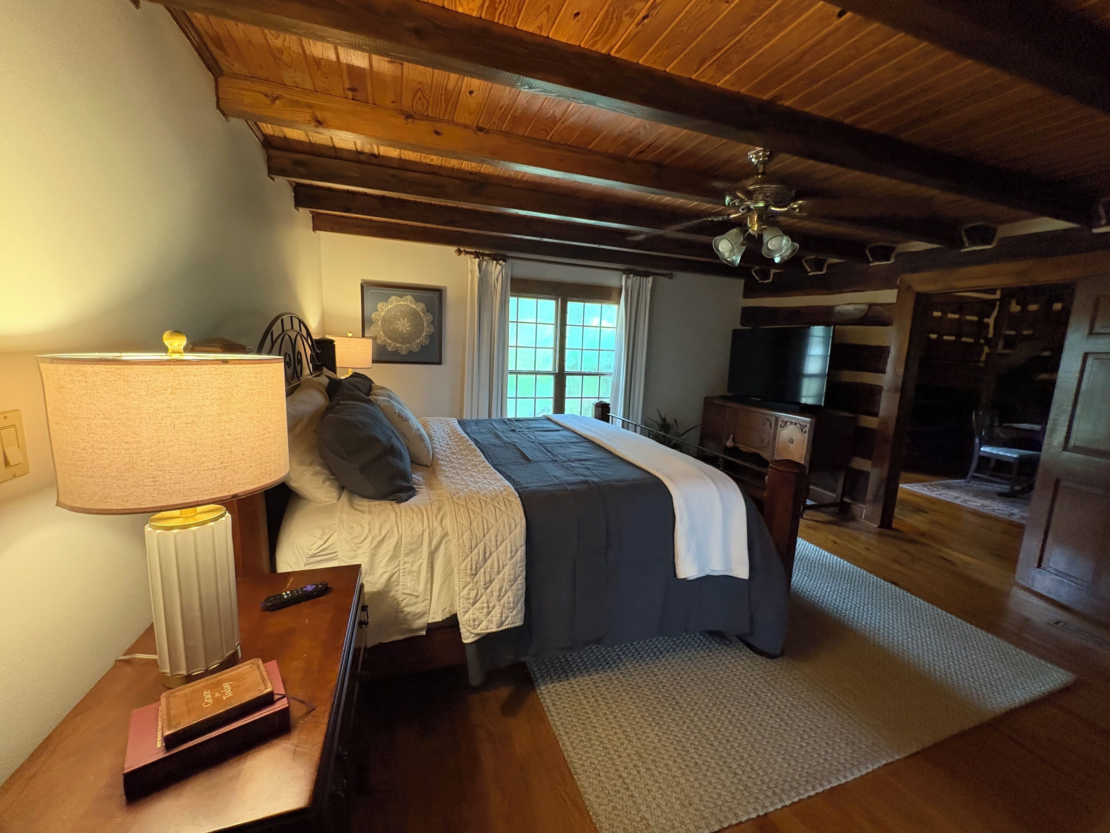 A bedroom with a bed, bedside table, lamp, and a ceiling fan.