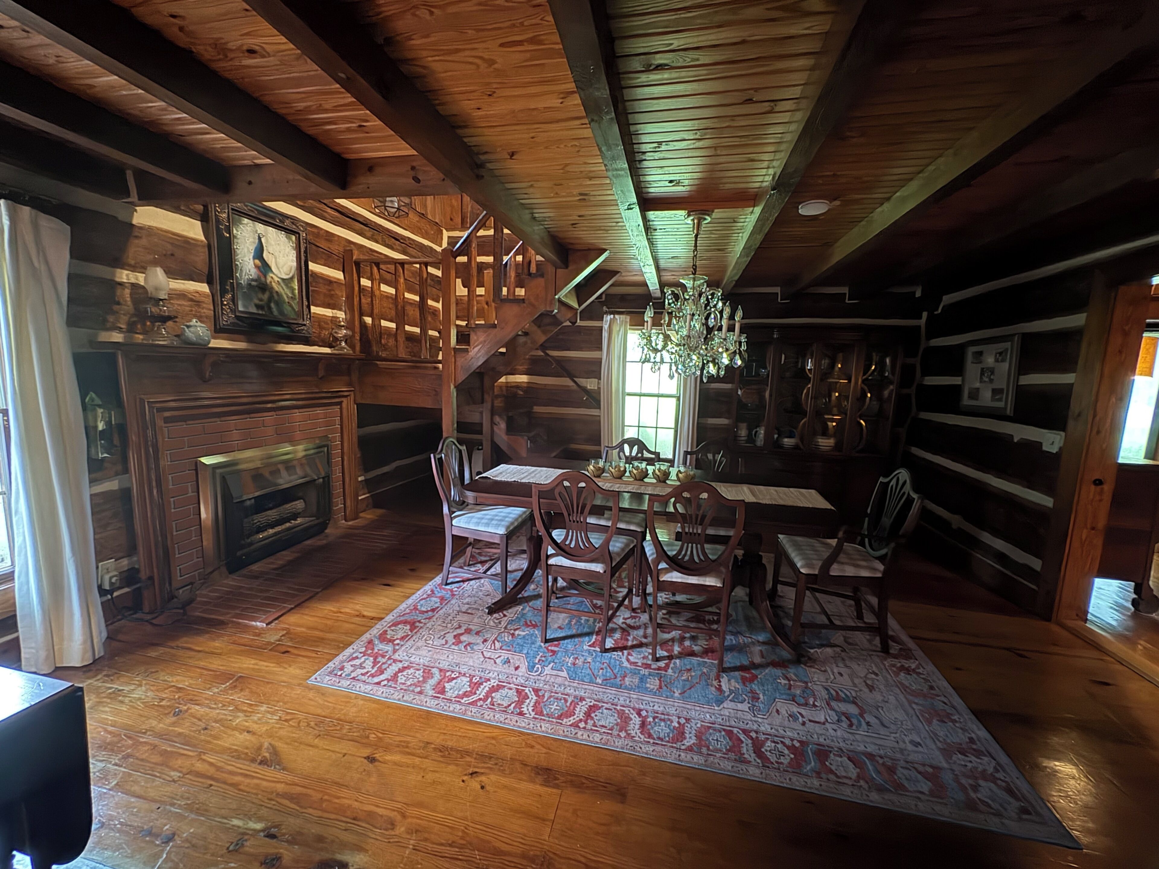 Un interno rustico con una scala in legno, una zona pranzo con tavolo e sedie, un camino e un lampadario.