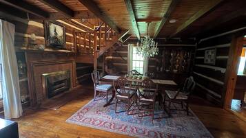 Un interno rustico con una scala in legno, una zona pranzo con tavolo e sedie, un camino e un lampadario.