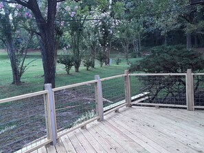 A wooden deck with a metal fence overlooking a grassy area with trees and shrubs.