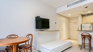 A compact room with a bed, a TV, a dining table with chairs, and a kitchenette. - Suite w/ Pool View in Luxury Resort Jurere Jbv348 (Florianópolis)