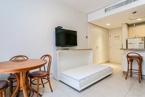 Ein gemütliches Zimmer mit Bett, Fernseher, Esstisch mit Stühlen und einer Küchenzeile.
