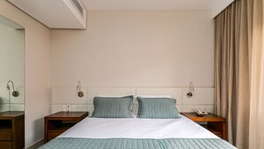 A hotel room with a large bed, two bedside tables, a nightstand, a mirror, and a window with curtains. - Suite w/ Pool View in Luxury Resort Jurere Jbv348 (Florianópolis)