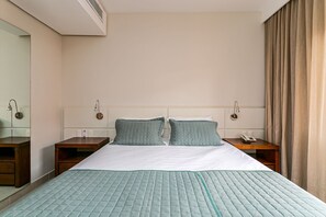 Ein Hotelzimmer mit einem großen Bett, zwei Nachttischen, einem Schminktisch und einem Fenster mit Vorhängen.