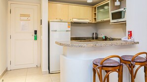 A kitchen with a refrigerator, microwave, and granite countertop. There are three wooden chairs with cushioned seats. - Suite w/ Pool View in Luxury Resort Jurere Jbv348 (Florianópolis)