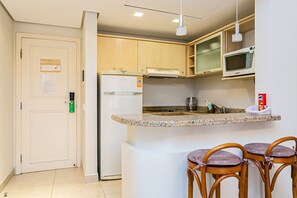 Eine Küche mit Kühlschrank, Mikrowelle und einer Arbeitsplatte aus Granit. Es sind drei Holzstühle mit gepolsterten Sitzen vorhanden.