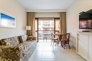 A hotel room with a sofa, a TV, a dining table with chairs, and a balcony with a view of buildings. - Suite w/ Pool View in Luxury Resort Jurere Jbv348 (Florianópolis)