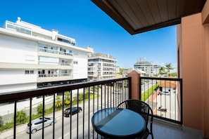Een balkon met een tafel en stoelen, met uitzicht op een straat met auto's en gebouwen.