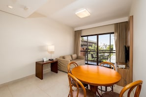 A hotel room with a balcony, a sofa, a dining table with chairs, a TV, and a desk with a lamp. - Spectacular Suite in a Luxurious Resort Jbv179 (Florianópolis)