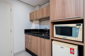 Uma cozinha compacta com armários de madeira, bancada preta, micro-ondas e geladeira compacta.