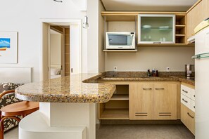 A kitchen with a granite countertop, wooden cabinets, a microwave, and a refrigerator. - Suite W/beautiful View in Resort in Jurere Jbv252 (Florianópolis)