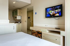 A hotel room with a bed, a desk with two chairs, a microwave, and a television mounted on the wall. - Sea View in a Beachfront Resort Jbv465 (Florianópolis)