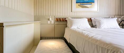 Una habitación de hotel con cama, mesita de noche, una lámpara y un cuadro en la pared, además de un ventanal.