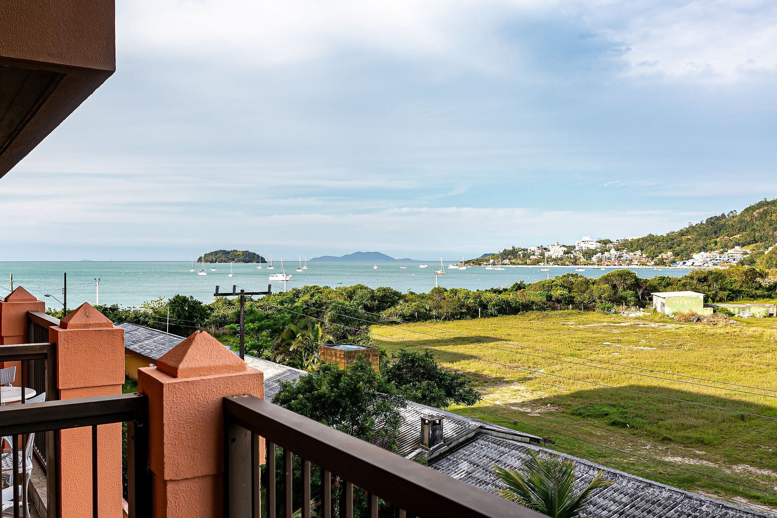 Ein Balkon mit Blick auf eine Küstenlandschaft, darunter Schiffe auf dem Wasser und eine Wiese.