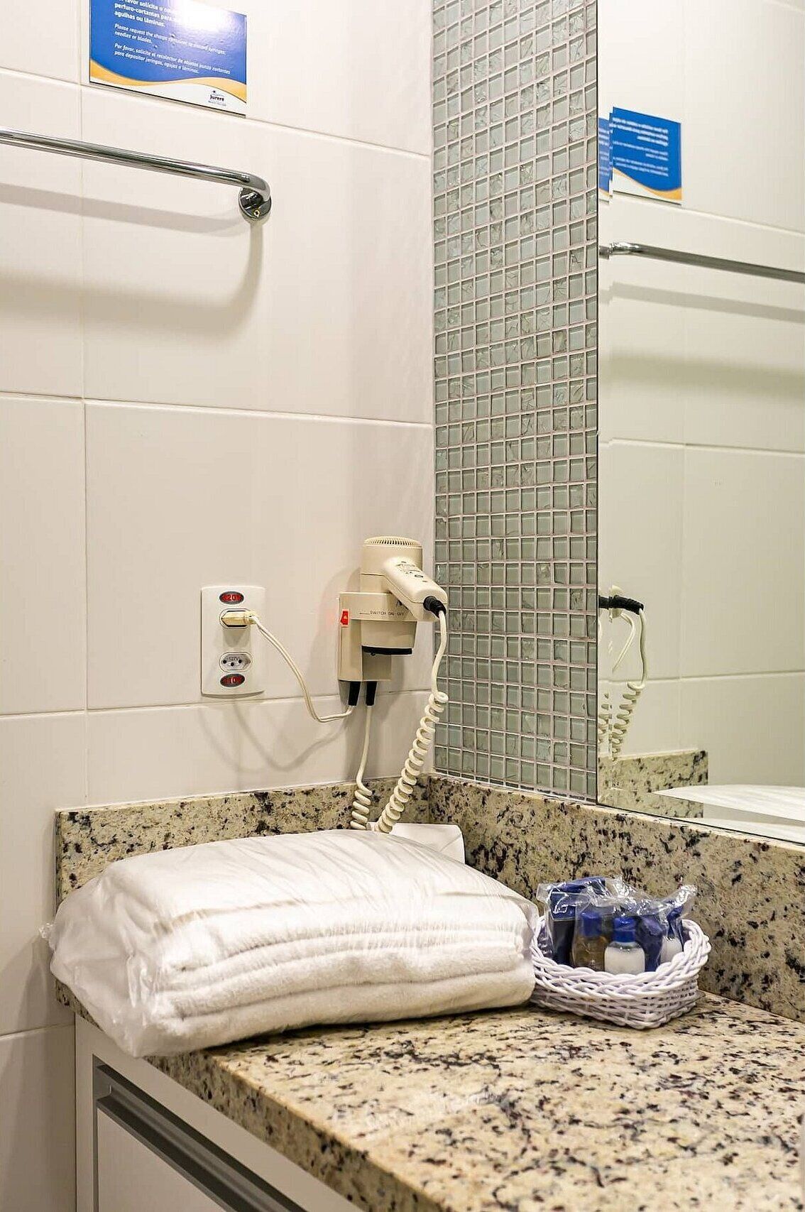 A bathroom with a granite countertop, a towel, a basket, and a hairdryer plugged into a wall outlet.