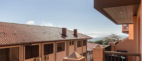 A residential building with a tiled roof, multiple windows, and a balcony overlooking a cityscape and distant mountains.